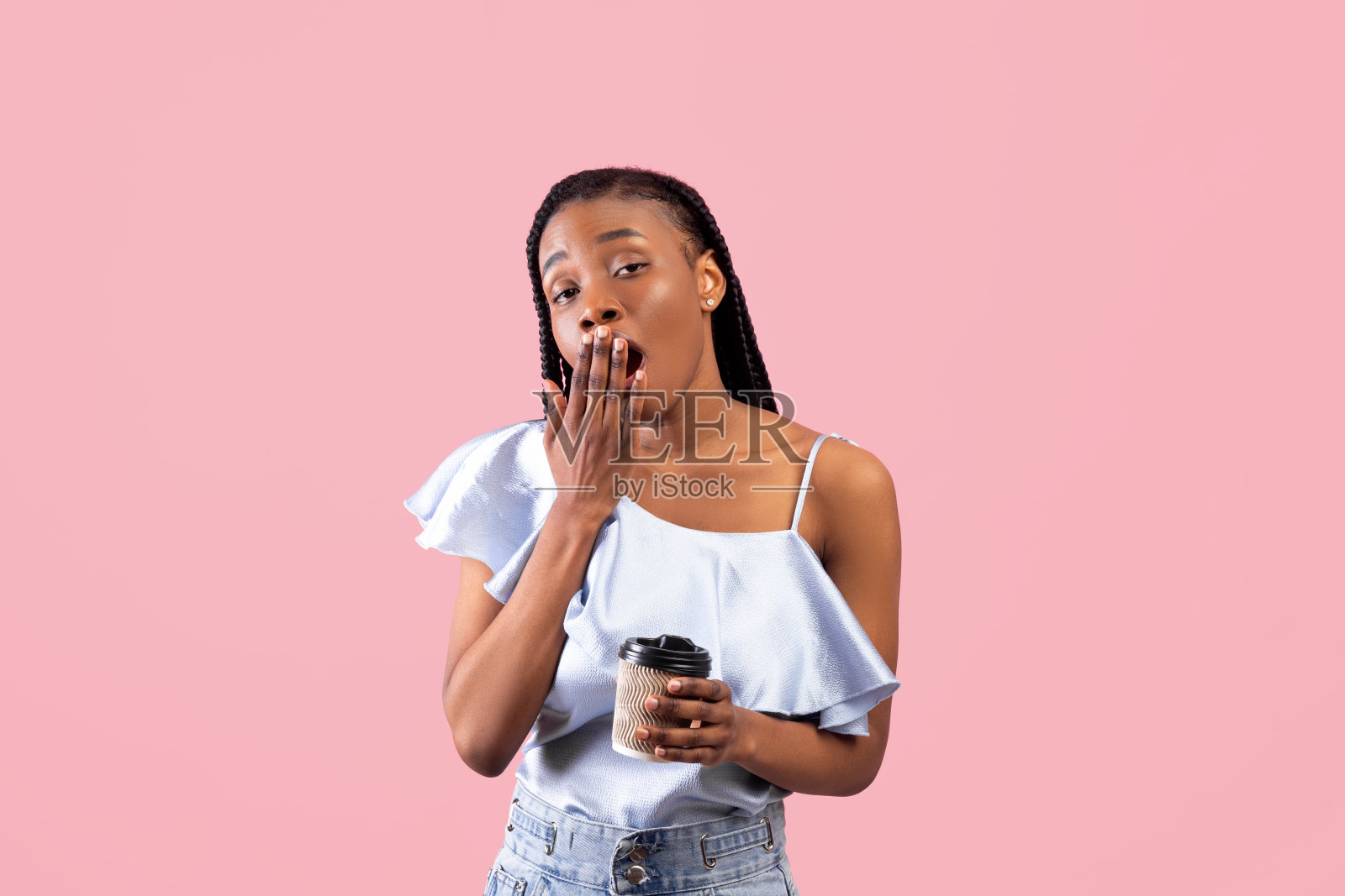 疲倦的非洲裔美国女人拿着纸杯外卖咖啡和打哈欠在粉红色的工作室背景照片摄影图片