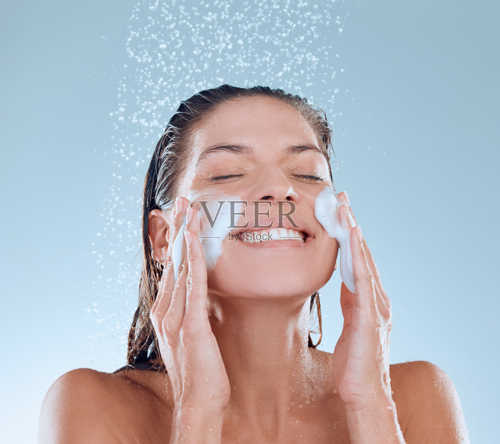 一名年轻女子在淋浴时洗脸，背景为蓝色照片摄影图片