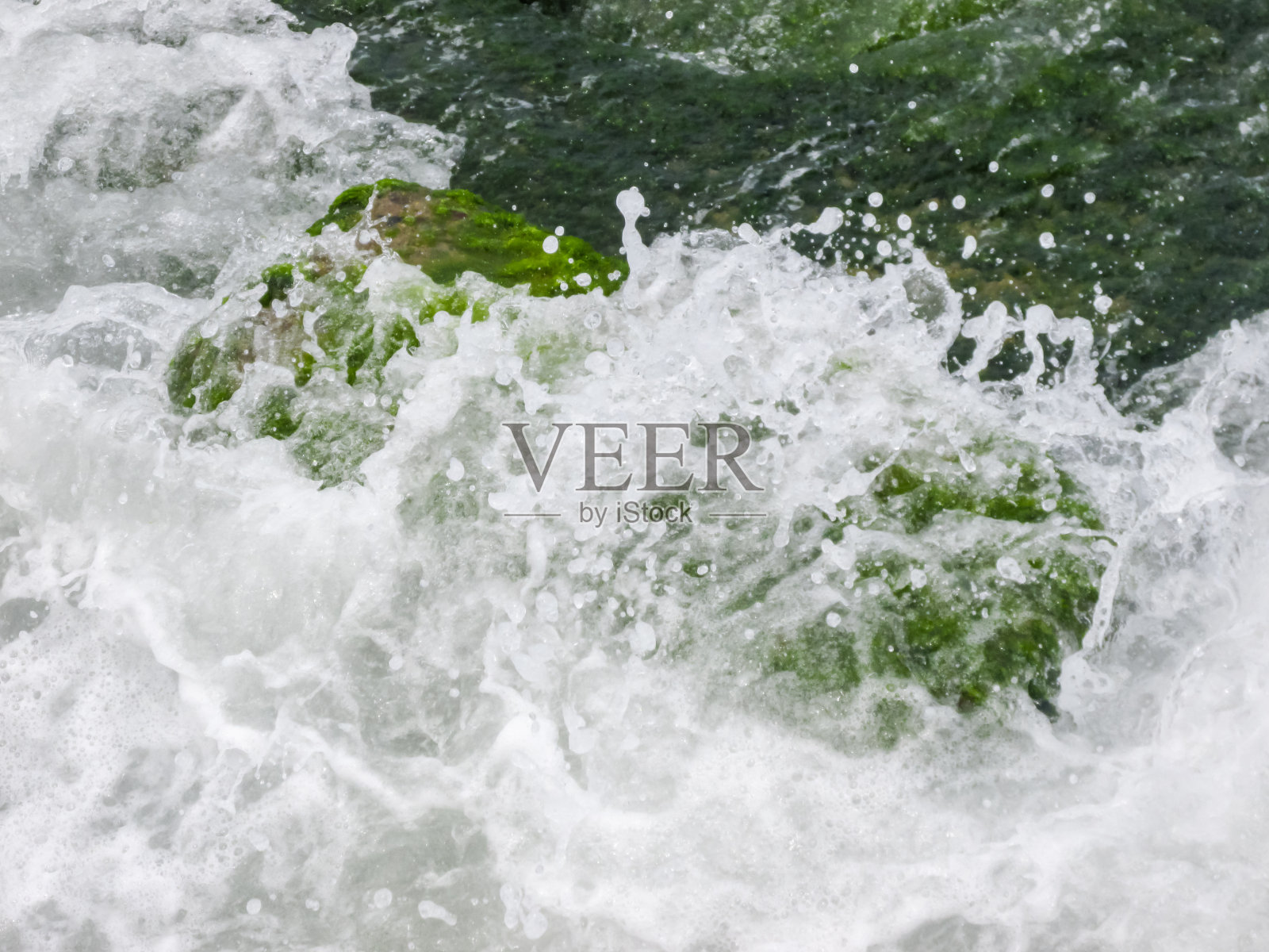 一个浪头打在堤坝上长满青苔的石头上照片摄影图片