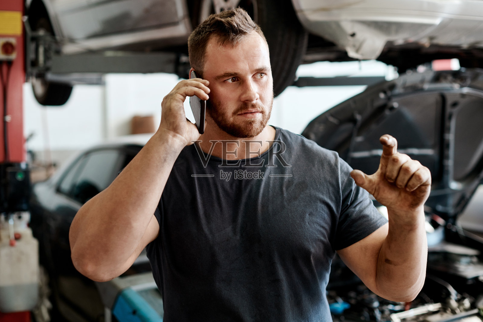 图为一名修理工在汽车修理店工作时打电话照片摄影图片