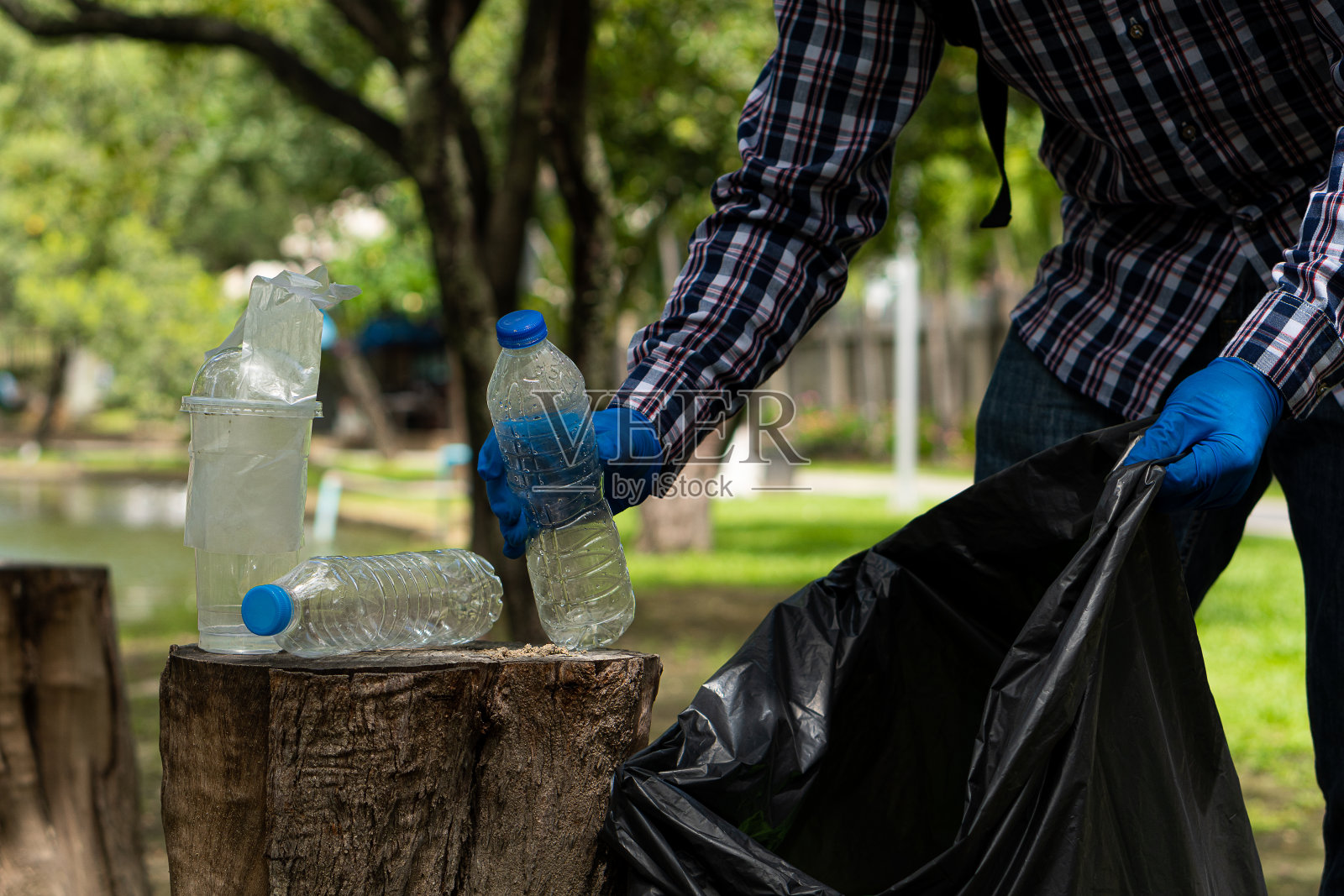 在公园的垃圾收集志愿者活动中，志愿者在公园收集可回收的塑料瓶。快乐的人用黑色的袋子打扫。生态的概念照片摄影图片