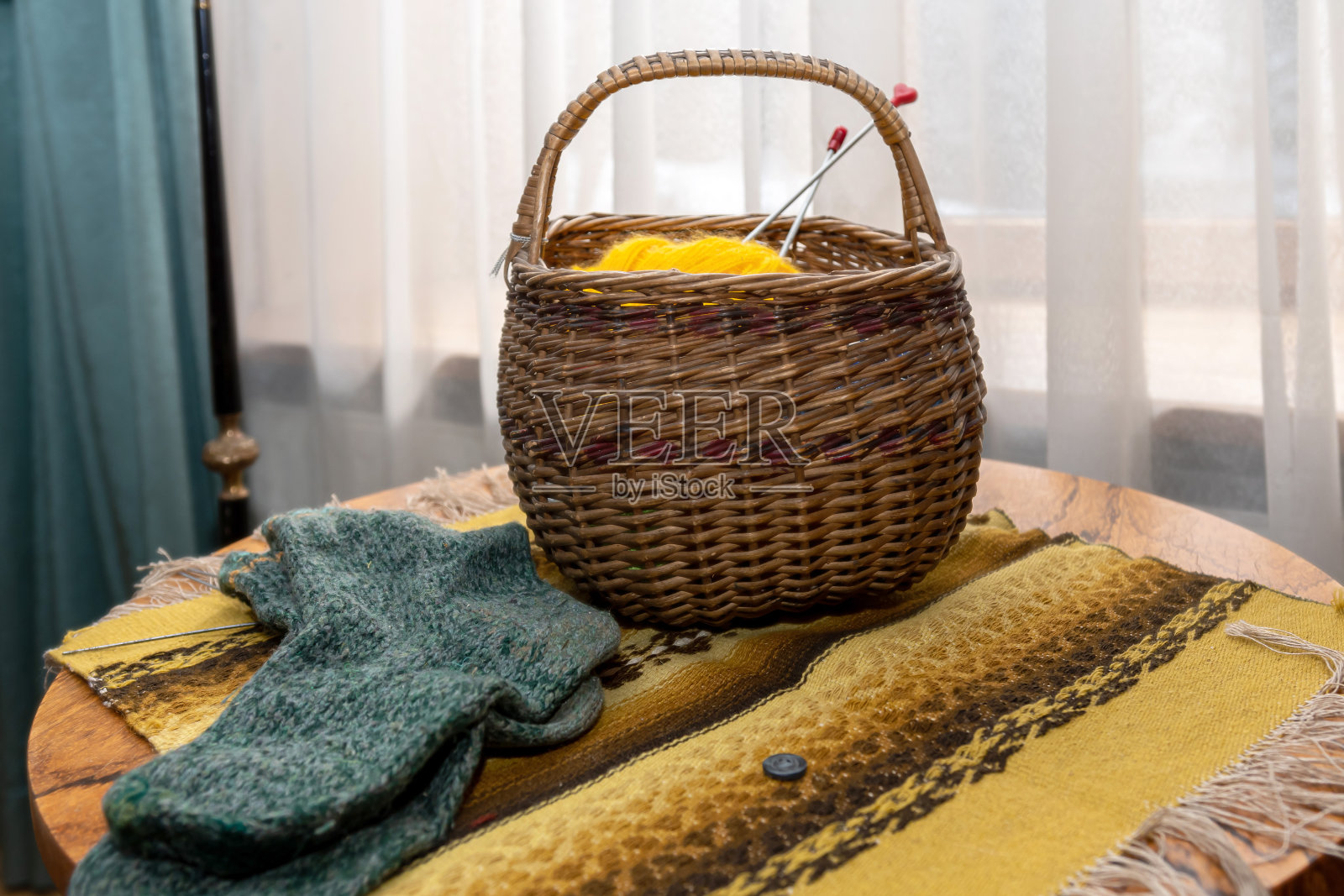 复古的室内装饰，编织的袜子和用纱线编成的柳条篮子放在一张木制的圆桌上，上面盖着一条民间毯子照片摄影图片