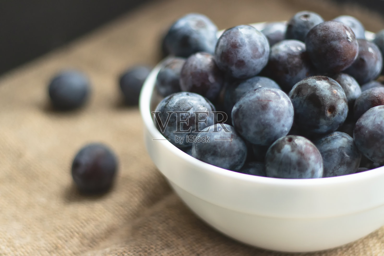 把成熟的甜李子放在白盘子里，放在粗麻布上照片摄影图片