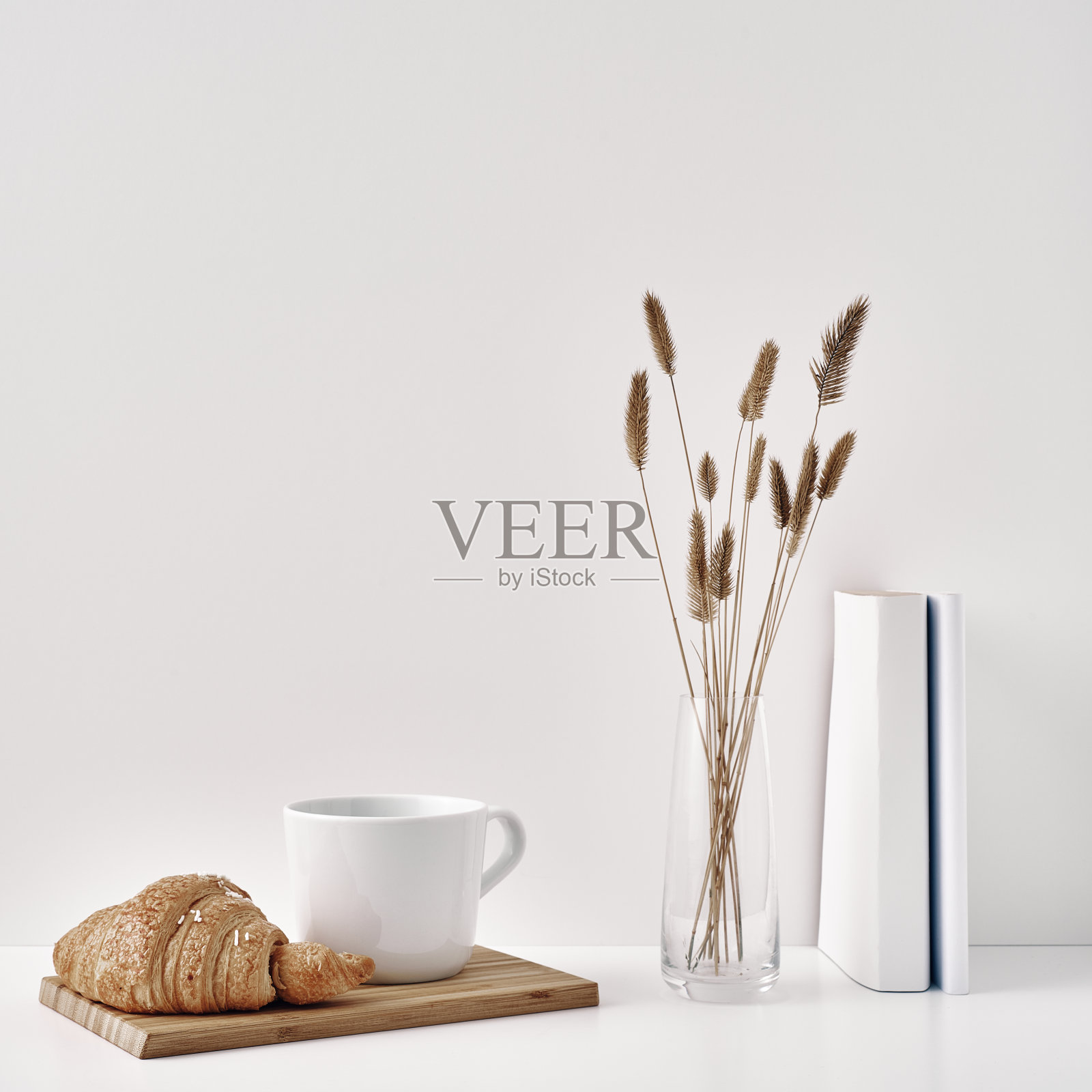 木架上放着羊角面包和一个马克杯，书上放着一个花瓶和一个盆栽，背景是白色的。室内装饰采用环保材料，极简主义。复制空间，模仿。照片摄影图片