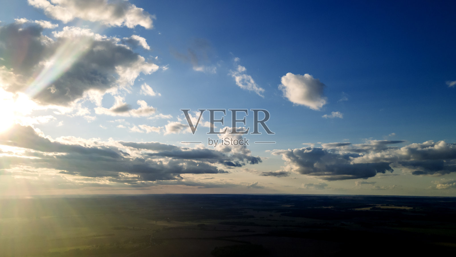 阳光透过天空中的云照耀着。令人惊奇的蓬松的云在天空上柔和地移动，太阳通过云闪耀着美丽的光线和透镜耀斑。空间的文本。照片摄影图片