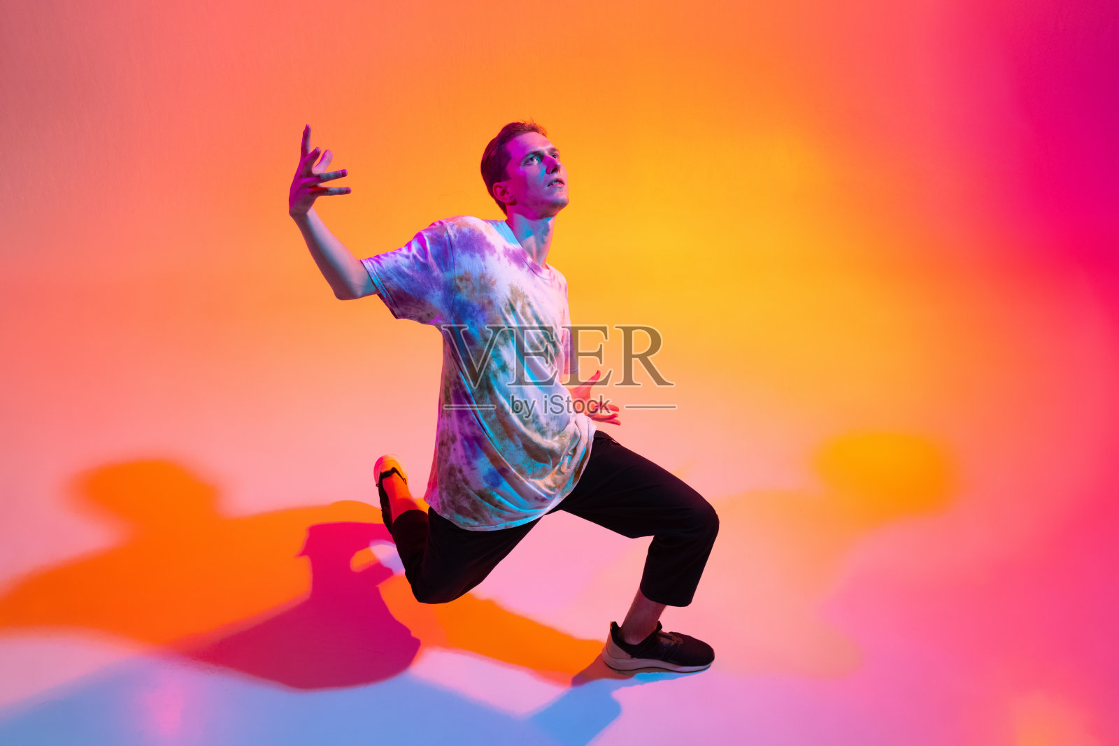 俯视图图像的年轻艺术男子跳舞嘻哈孤立在渐变的黄色粉红色工作室背景霓虹灯照片摄影图片