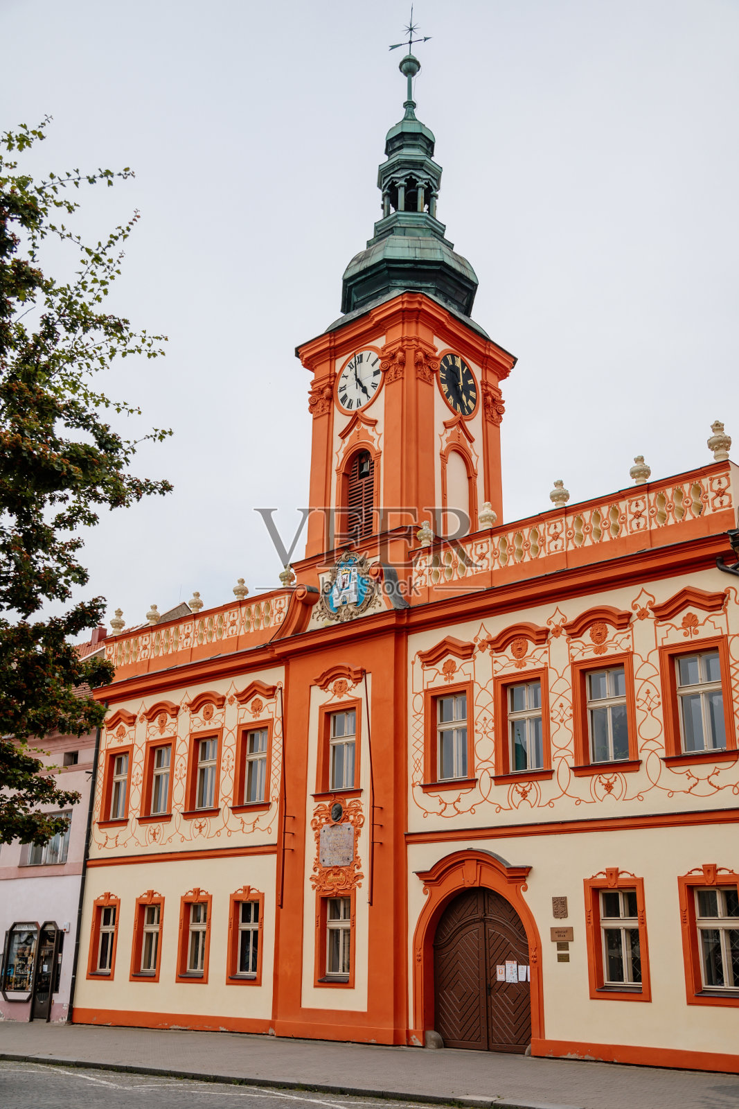 捷克共和国波西米亚中部地区拉科夫尼克，2021年6月19日:胡索夫广场主广场上的巴洛克式红色和米色市政厅，带有钟塔，入口上方有城市盾徽。照片摄影图片