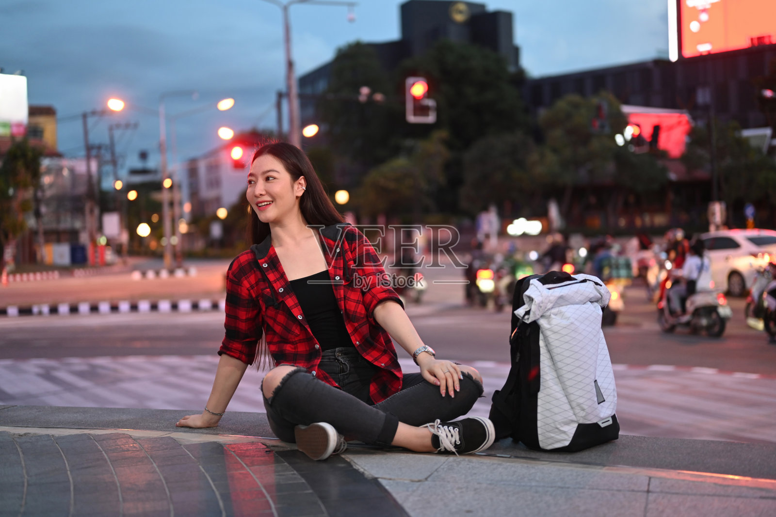 一个开朗的亚洲女人坐在夜晚的城市街道上。照片摄影图片