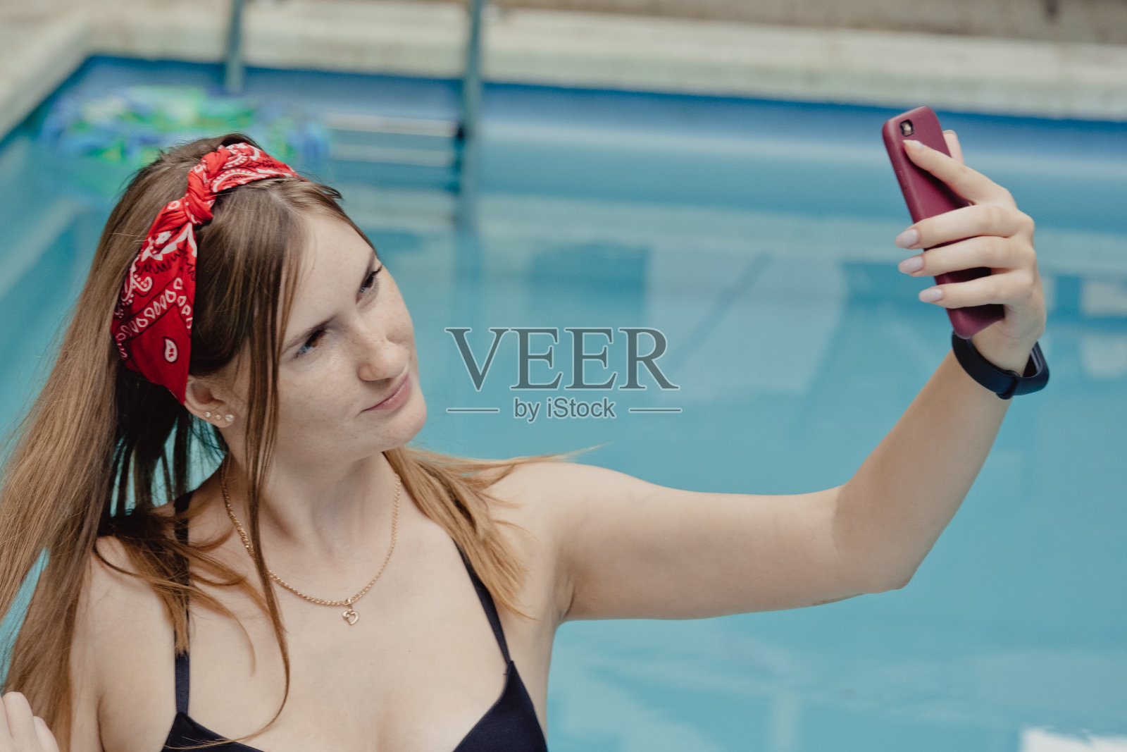 一个带着电话的微笑的年轻女人坐在躺椅上。放松水疗日在游泳池在夏天自拍照片或视频打电话给男朋友照片摄影图片