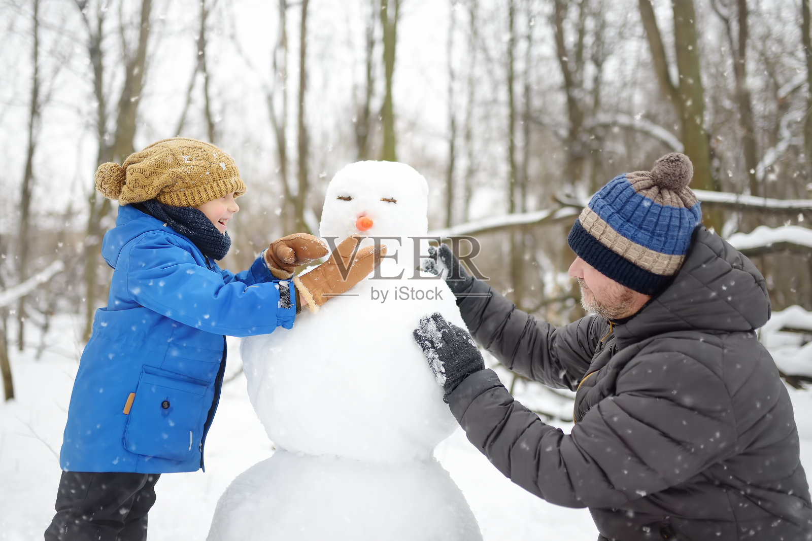 小男孩和他的父亲在下雪的公园堆雪人。冬季与孩子们一起活跃户外休闲活动。孩子在雪地里散步照片摄影图片