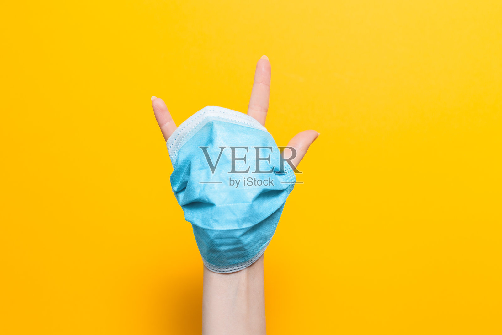 戴着面具手指伸出来的女人的手。黄色背景。本空间照片摄影图片