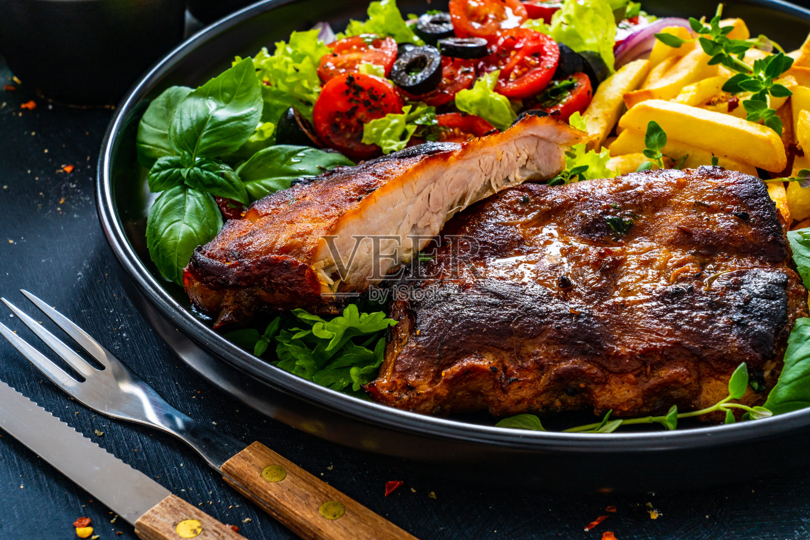 黑木桌上摆着烤排骨、炸薯条和番茄沙拉照片摄影图片