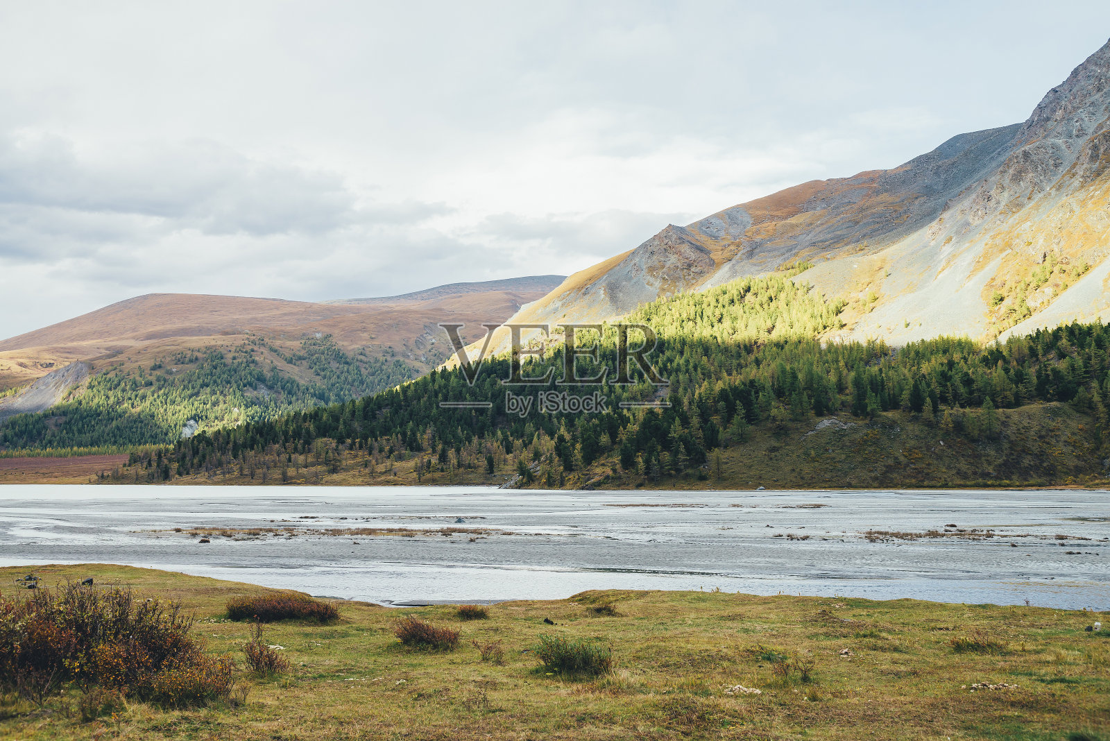 美丽的风景与溪水在山湖和阳光下斑驳的山在秋天的色彩。美丽的风景与秋天的植物，浅湖和山坡与森林在阳光下。照片摄影图片