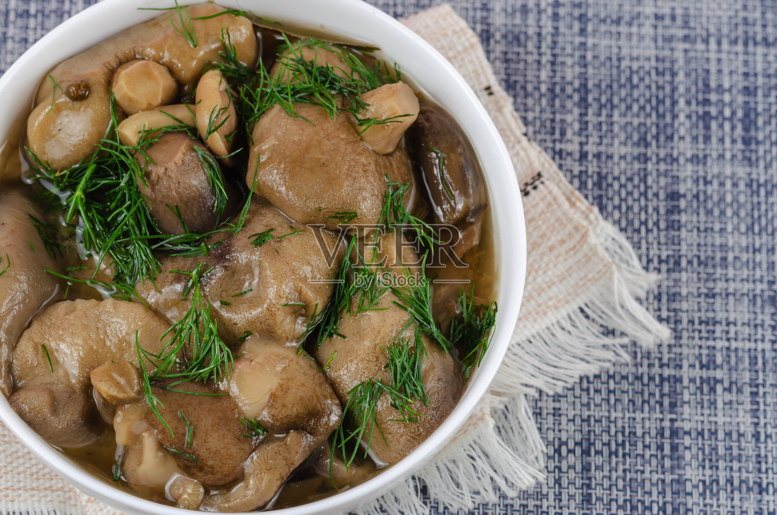 用白色陶瓷碗浸泡蘑菇，加入莳萝。白色的照片摄影图片