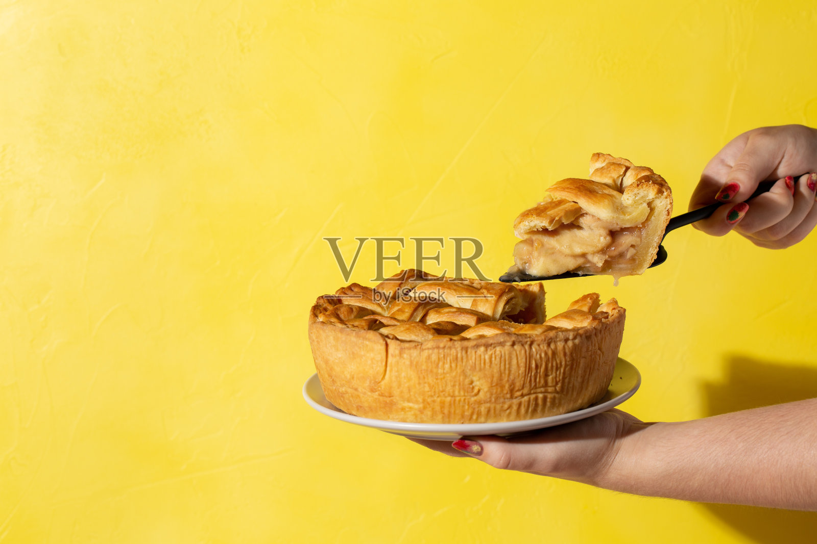 盘子与苹果派在女性手中明亮的黄色背景。感恩节的传统甜点。副本的空间。照片摄影图片