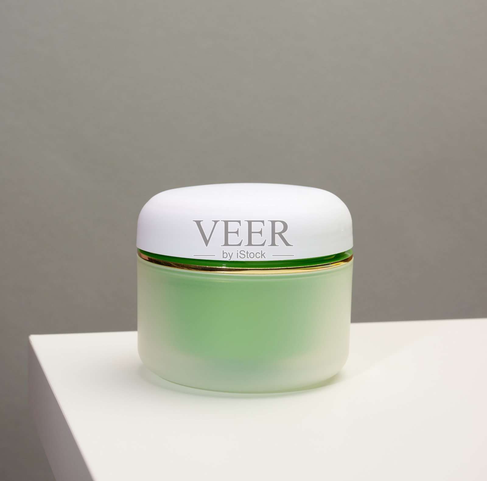 白色桌子上放着一个装化妆品的绿色罐子。包装霜，凝胶，血清，广告和产品推广，模拟照片摄影图片