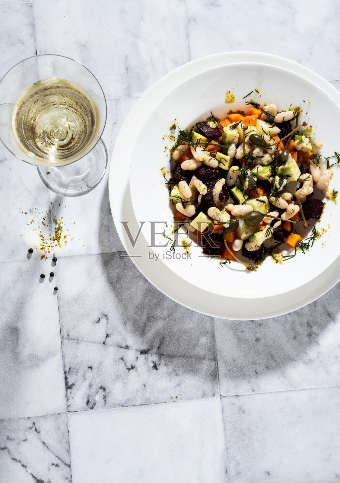 苏联菜醋汁蔬菜沙拉配甜菜和白豆。大理石桌上放着白葡萄酒照片摄影图片