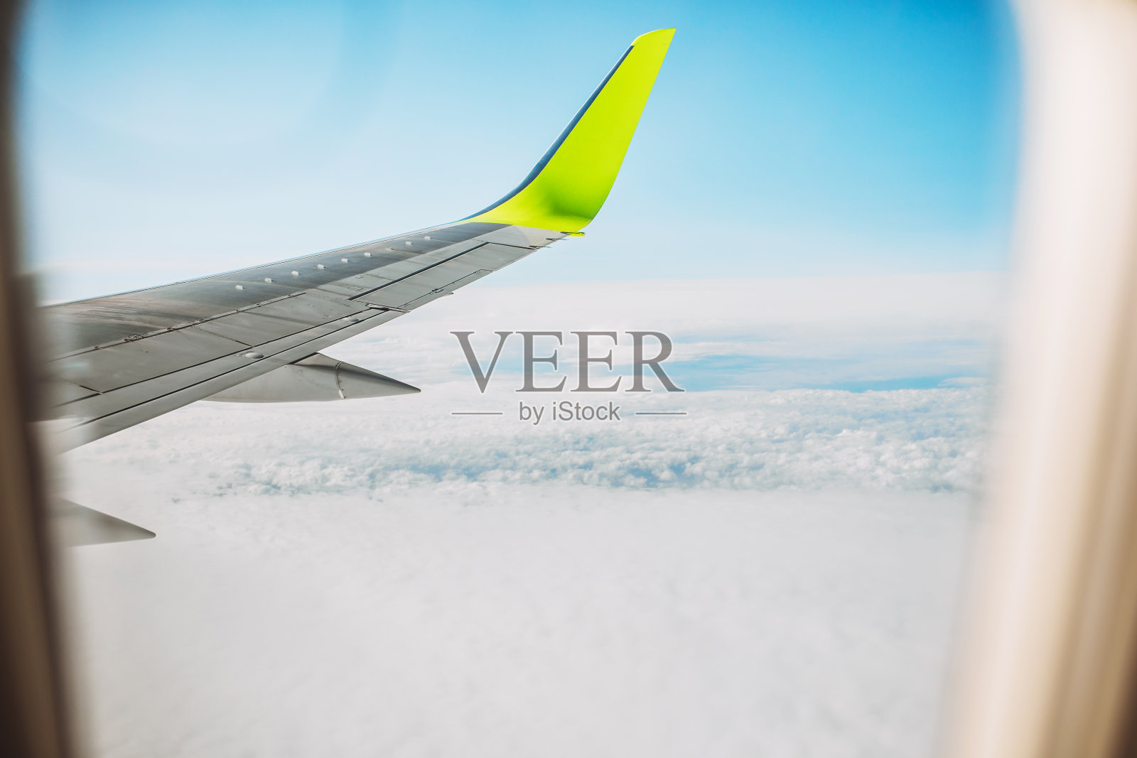 透过舷窗玻璃在云层上方飞行的飞机机翼的景象照片摄影图片