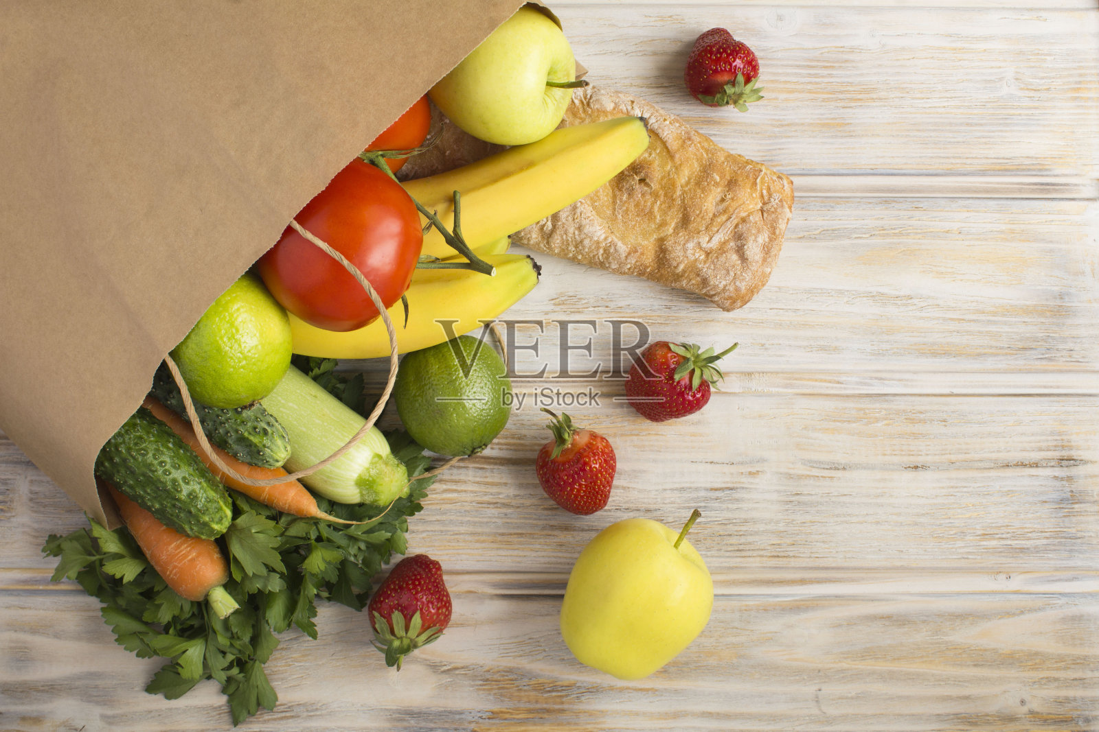 浅棕色木制背景上有蔬菜、水果和法棍的纸袋。前视图。副本的空间。照片摄影图片