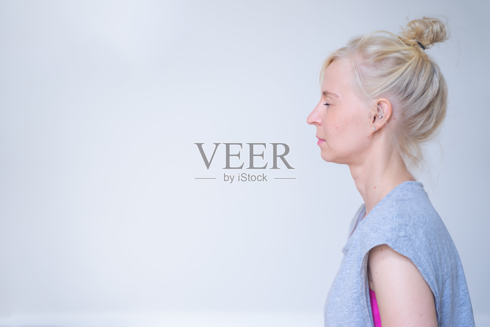 一位瑜伽教练闭着眼睛冥想的侧面，前面是一堵浅灰色的墙照片摄影图片