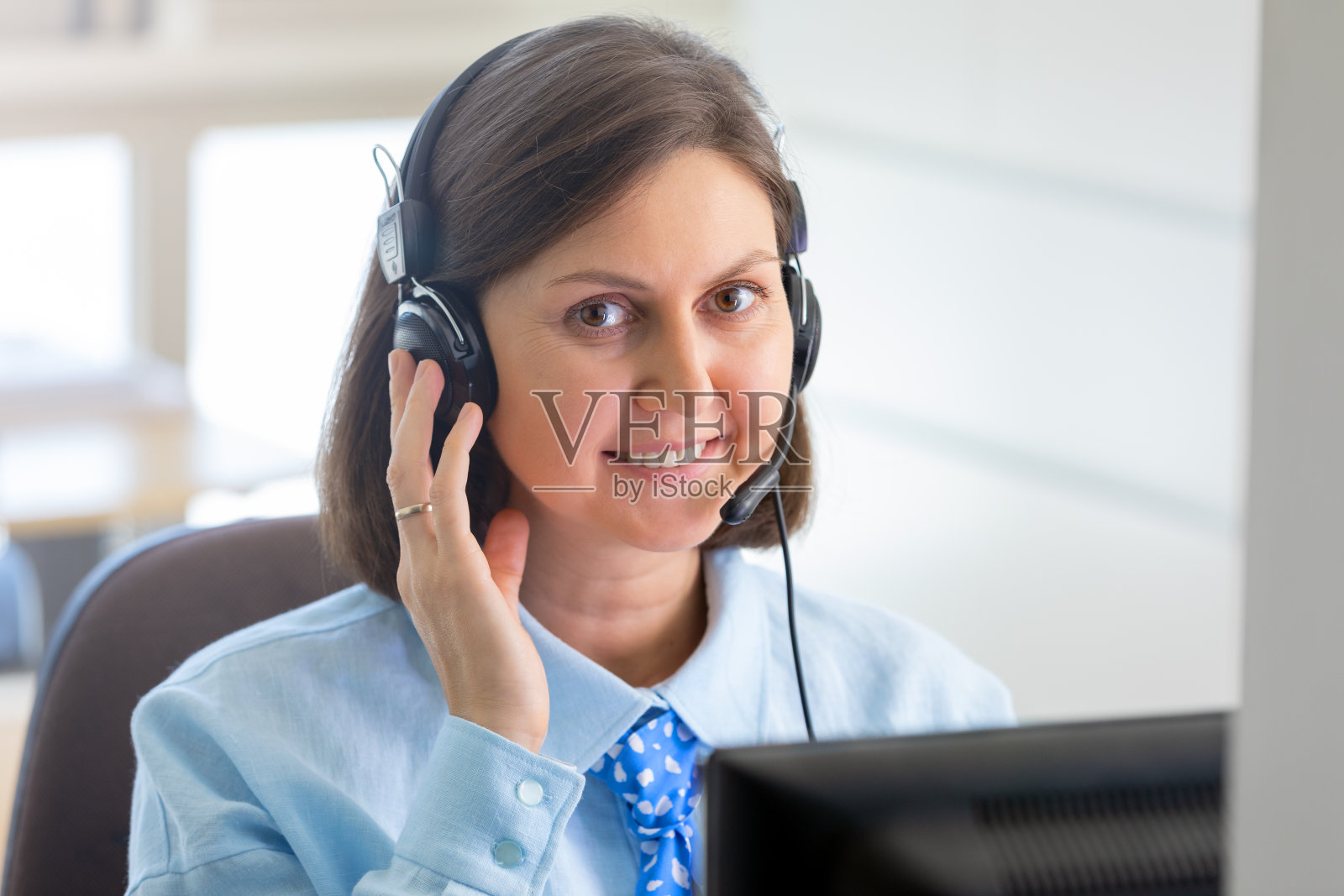 在办公室工作并使用电脑耳机与同事交谈的年轻女子肖像照片摄影图片