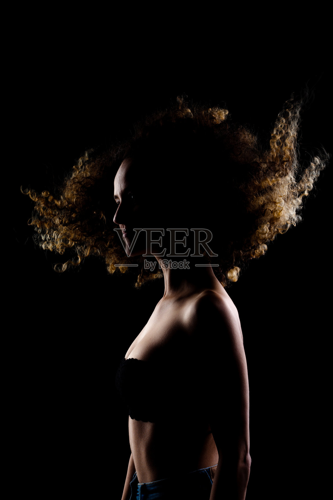 一边点燃黑发女孩与长卷发在空中。剪影工作室肖像在黑暗的背景。照片摄影图片