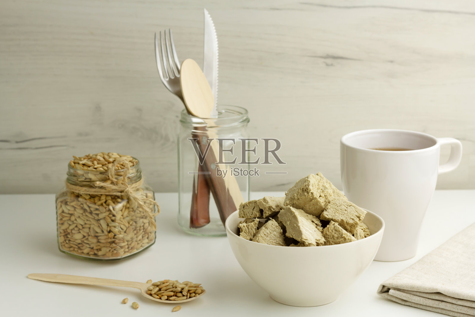 碗里放着向日葵，玻璃瓶里放着种子，浅色背景下放着一杯茶照片摄影图片