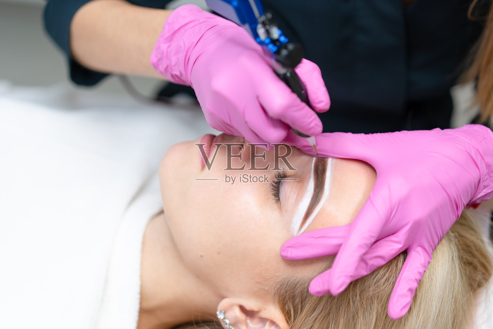 美容橱柜客户躺在沙发上。美容师在眉毛上做记号。照片摄影图片