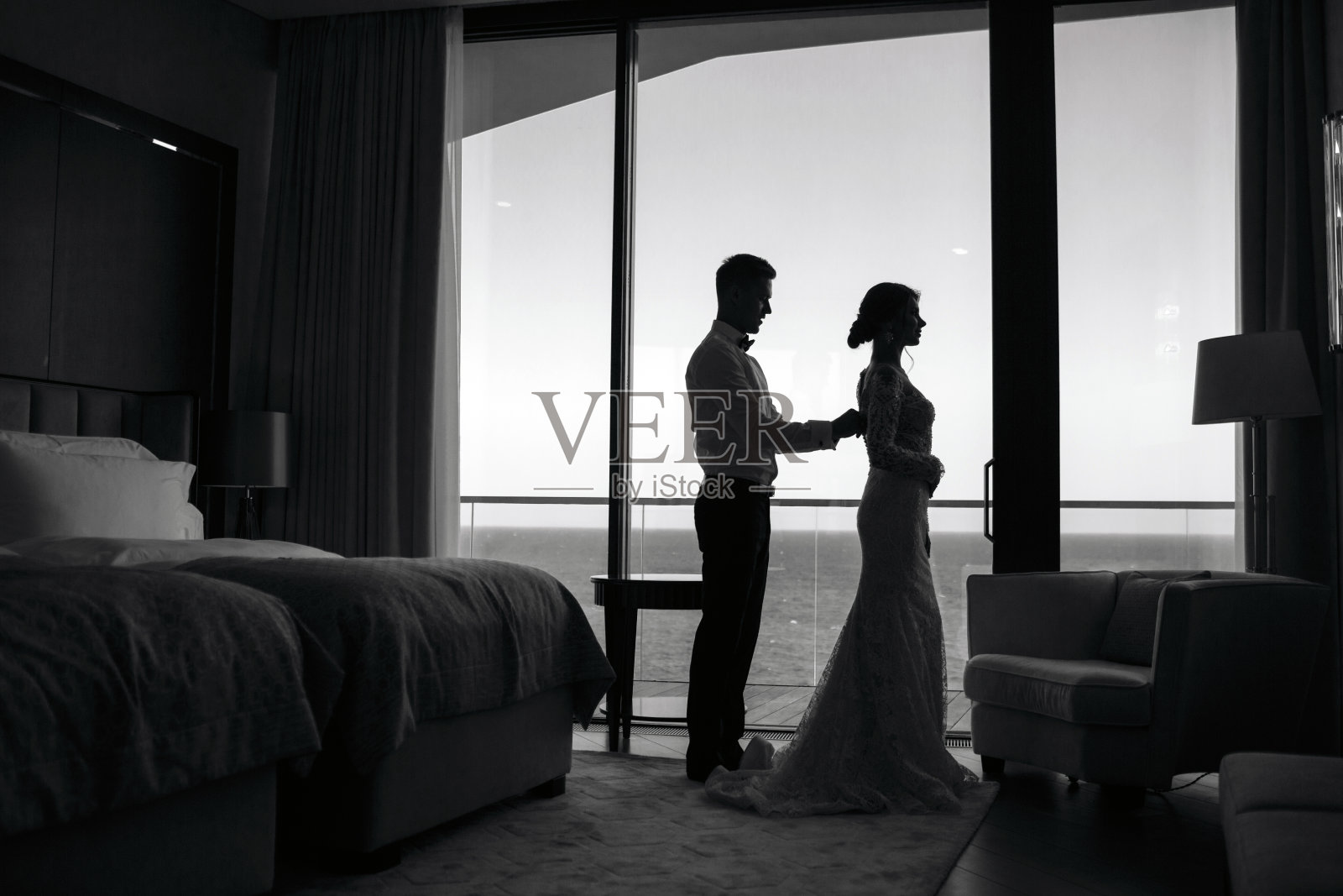 一个穿着白色礼服的美丽新娘和一个穿着白色衬衫的年轻新郎正在室内准备婚礼仪式。照片摄影图片