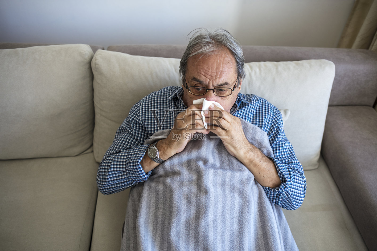 一位身体不适的老人躺在家里的沙发上擤鼻涕。照片摄影图片