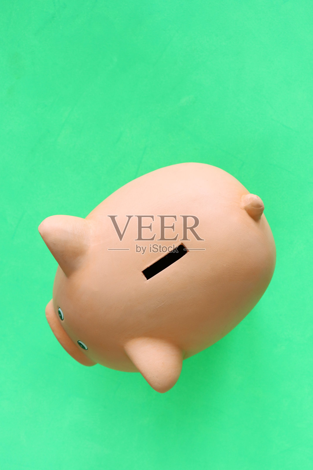 在绿色背景上坐在扑满后面的形象，高架的视野，抵押，家庭财务和储蓄的概念，复制空间照片摄影图片