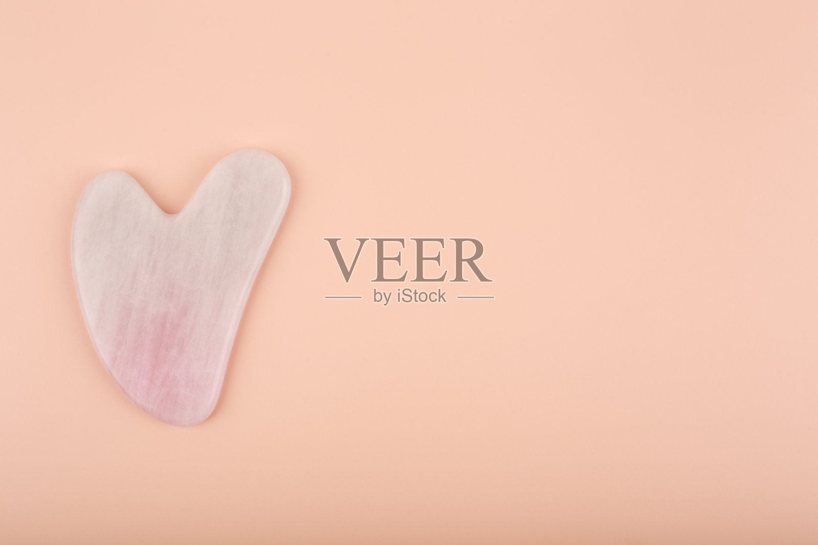 粉红色的心形瓜沙石由石英晶体制成，米色明亮的背景照片摄影图片