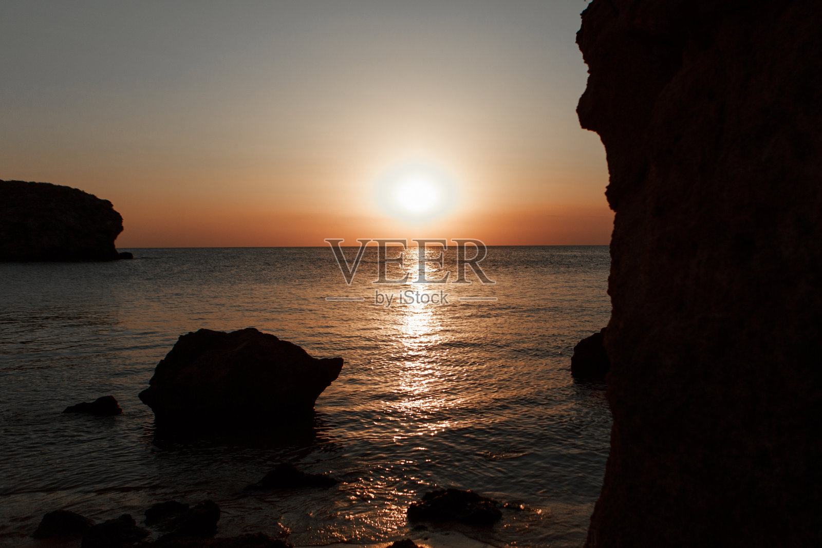 海浪冲刷着多岩石的海岸。日落。水中的倒影和桥上的光线照片摄影图片