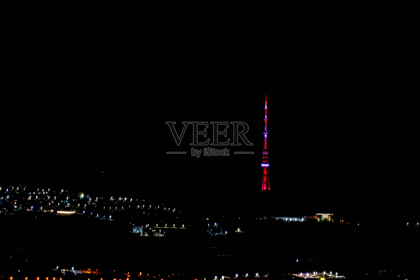 在寂静的夜晚，发光的电视塔。多色高塔和夜城的房屋。夜城里美丽的塔照片摄影图片