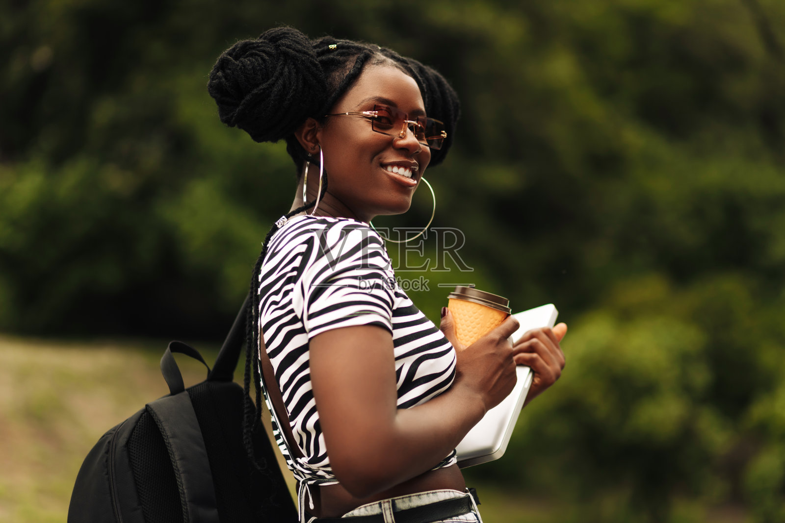 一个非洲女人，带着银色笔记本电脑走在户外，手里拿着咖啡外卖照片摄影图片