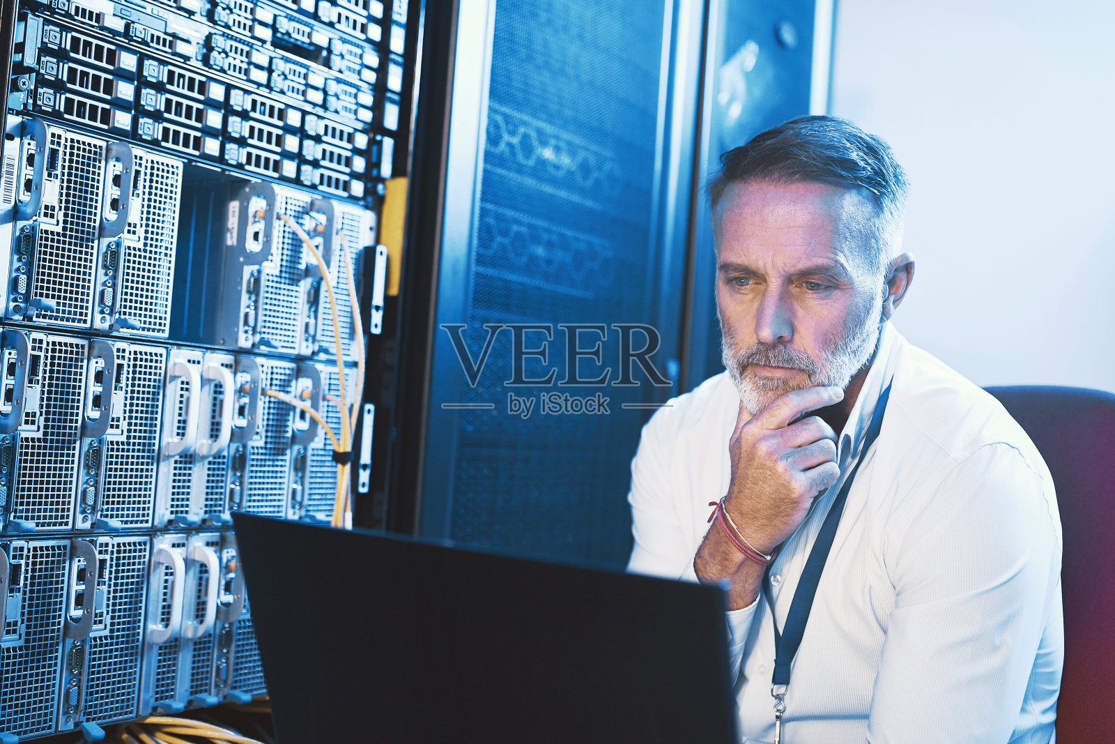 一名成熟男子在服务器室使用笔记本电脑，看上去若有所思照片摄影图片