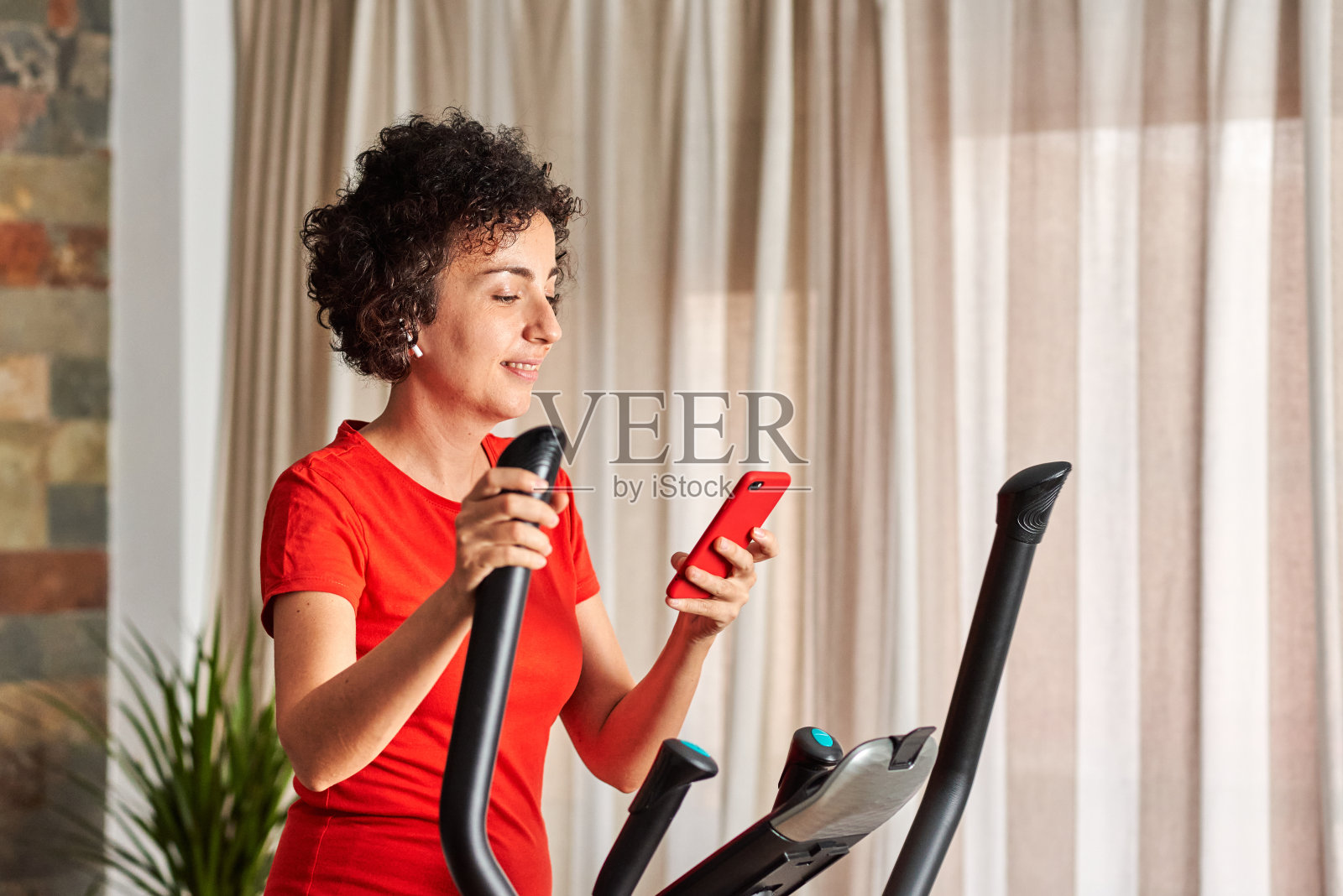 妇女在家里使用移动电话在交叉训练椭圆机上锻炼照片摄影图片