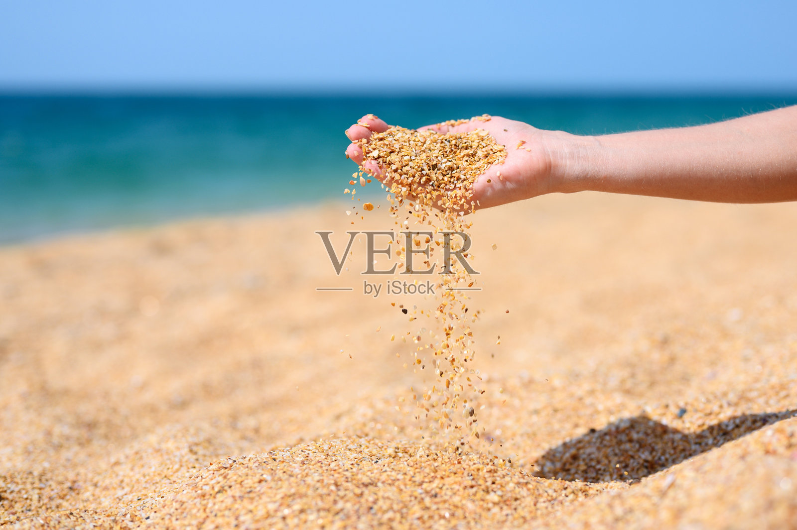 在沙滩和大海的映衬下，贝壳中的粗沙从女孩的手掌中流出。照片摄影图片