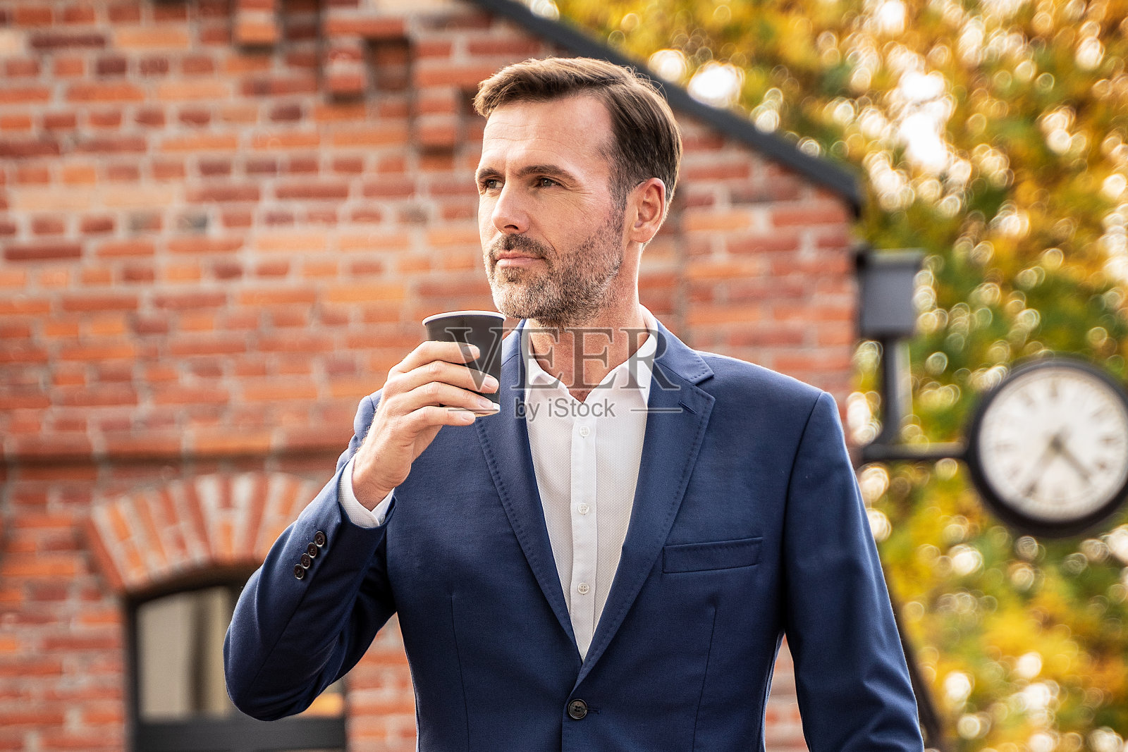 优雅帅气的商人带着纸制咖啡杯下班后在城市街道上。照片摄影图片