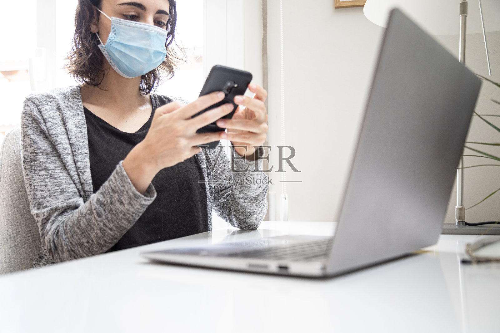 戴着面具的女孩看着手机和电脑工作照片摄影图片