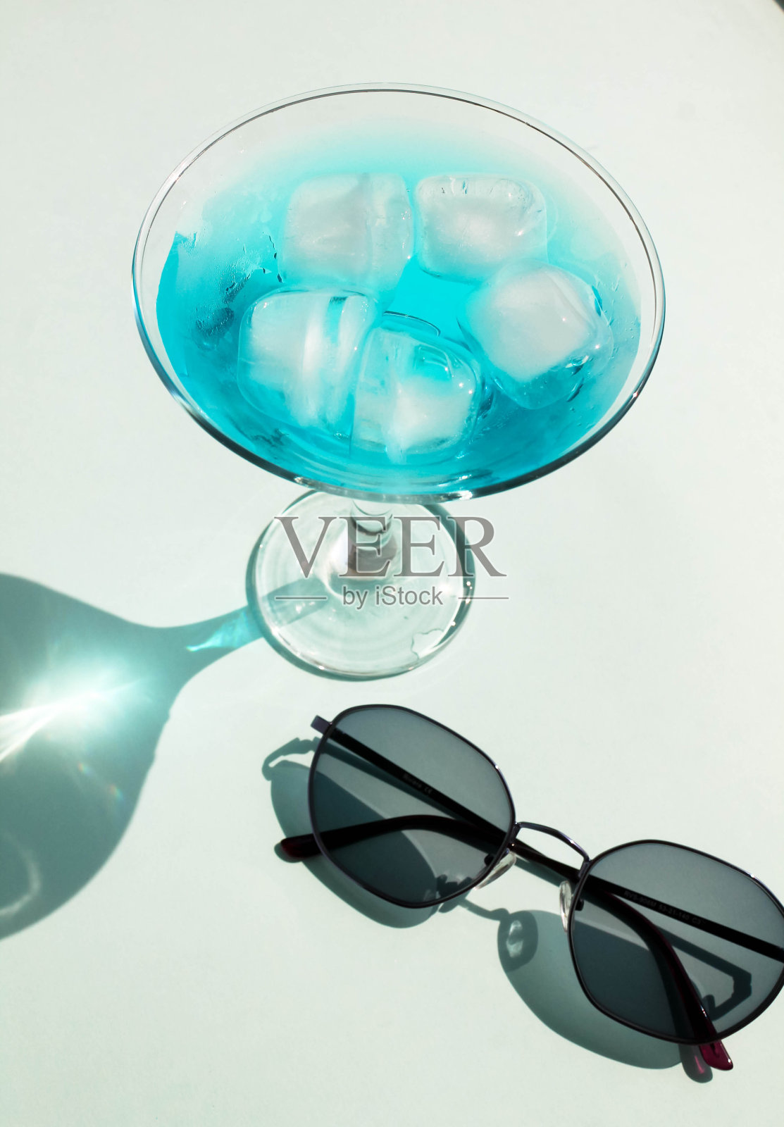 蓝色鸡尾酒与冰和太阳镜在灰白色的背景，俯视图，硬阴影照片摄影图片