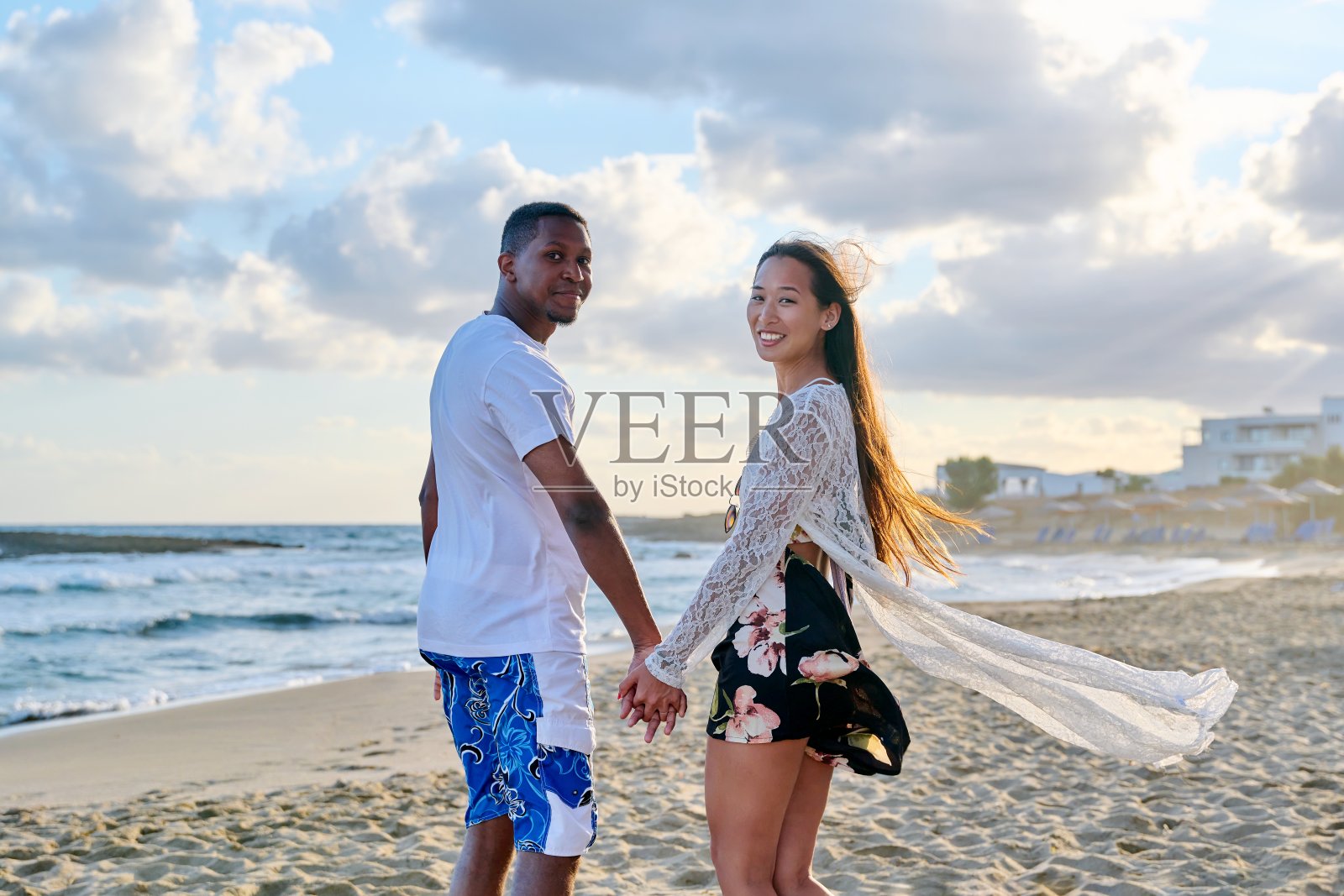 幸福的多民族年轻夫妇在海边手牵着手的肖像照片摄影图片