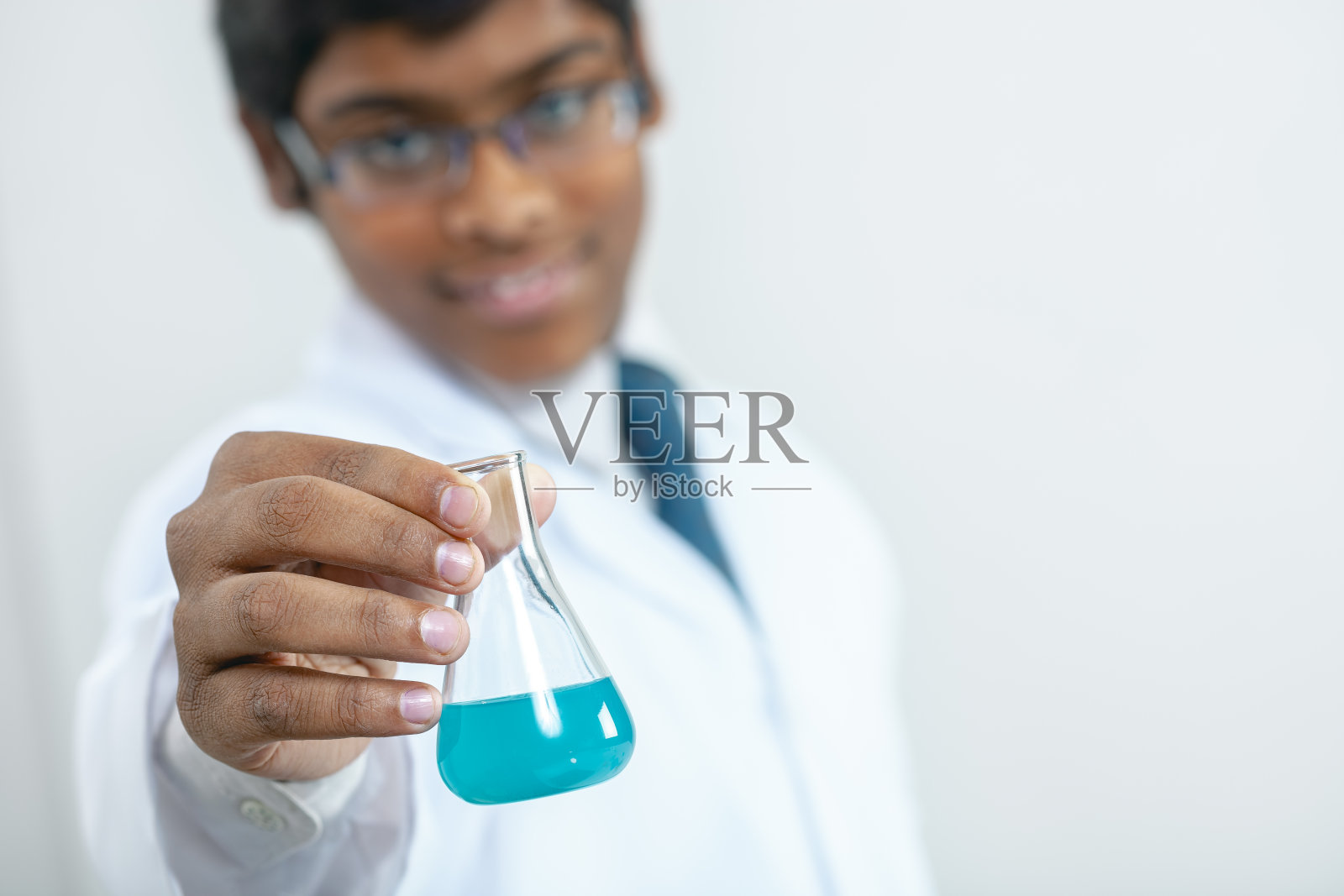 快乐的理科学生拿着一个装满蓝色化学物质的烧瓶。照片摄影图片