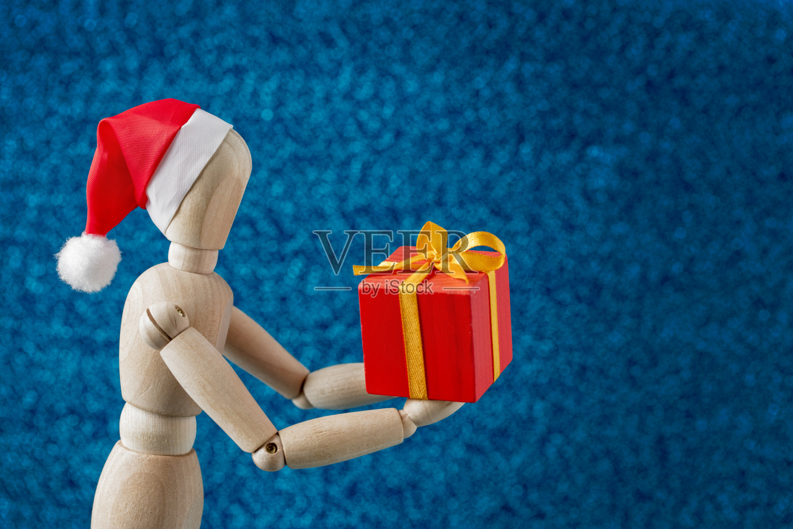 圣诞礼物-木制假人在圣诞老人的帽子拿着一个礼盒照片摄影图片
