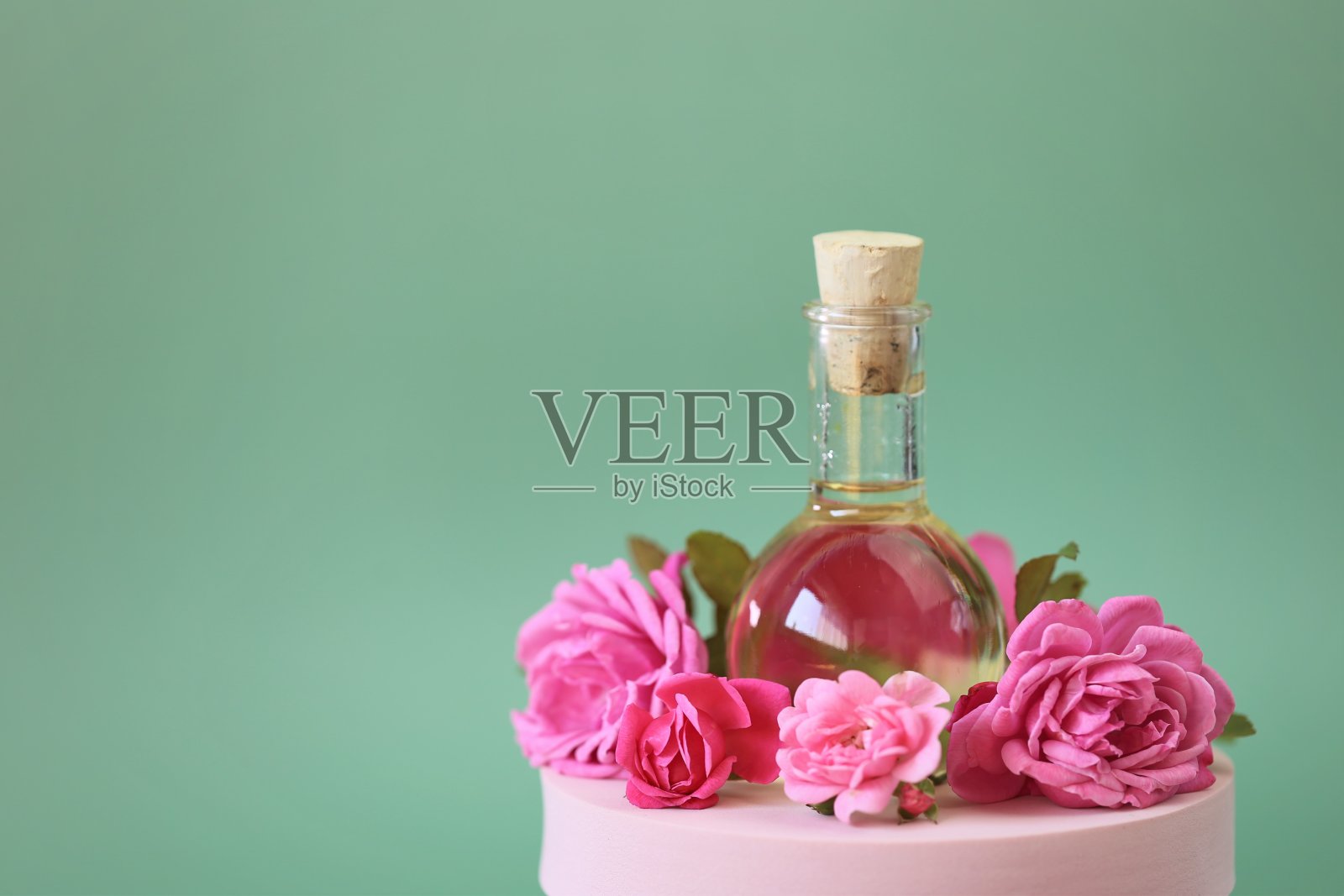 必要的玫瑰油。芳香疗法和按摩。玫瑰油和粉红色的玫瑰放在粉红色的讲台上浅绿色的背景。玫瑰精油。有机生物化妆品。照片摄影图片