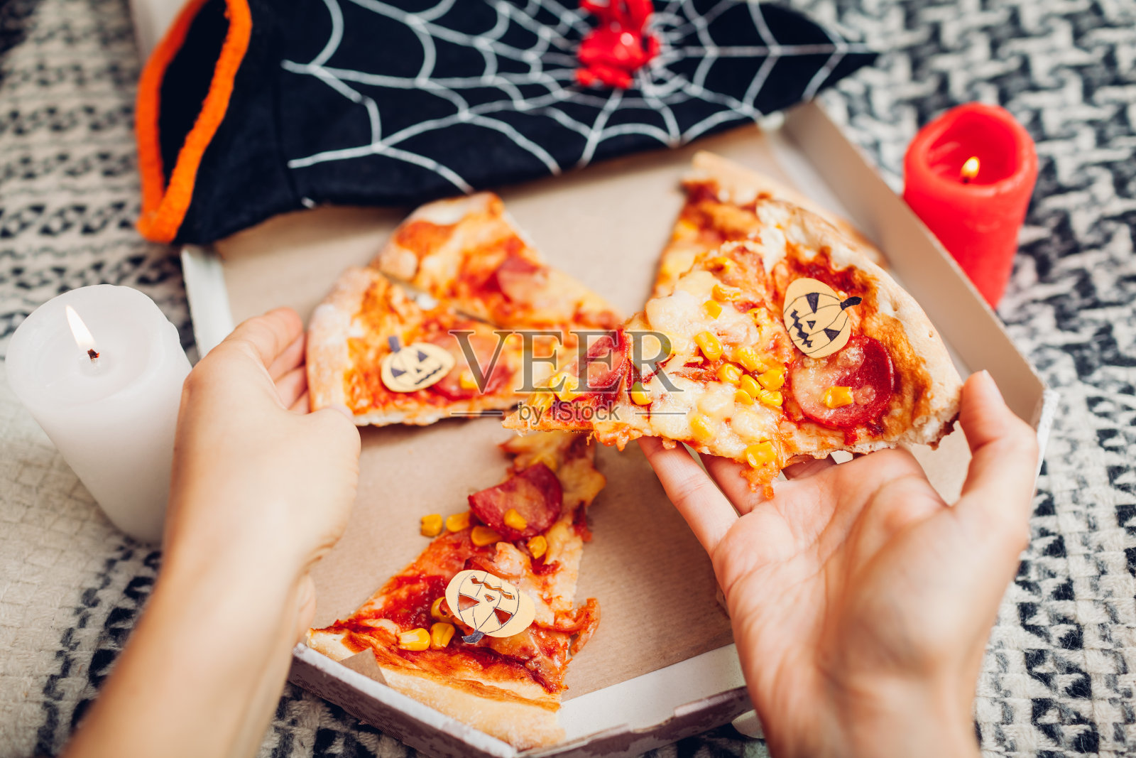 万圣节披萨，上面有小纸南瓜灯。有蜡烛和服装的节日派对。人们在食物照片摄影图片