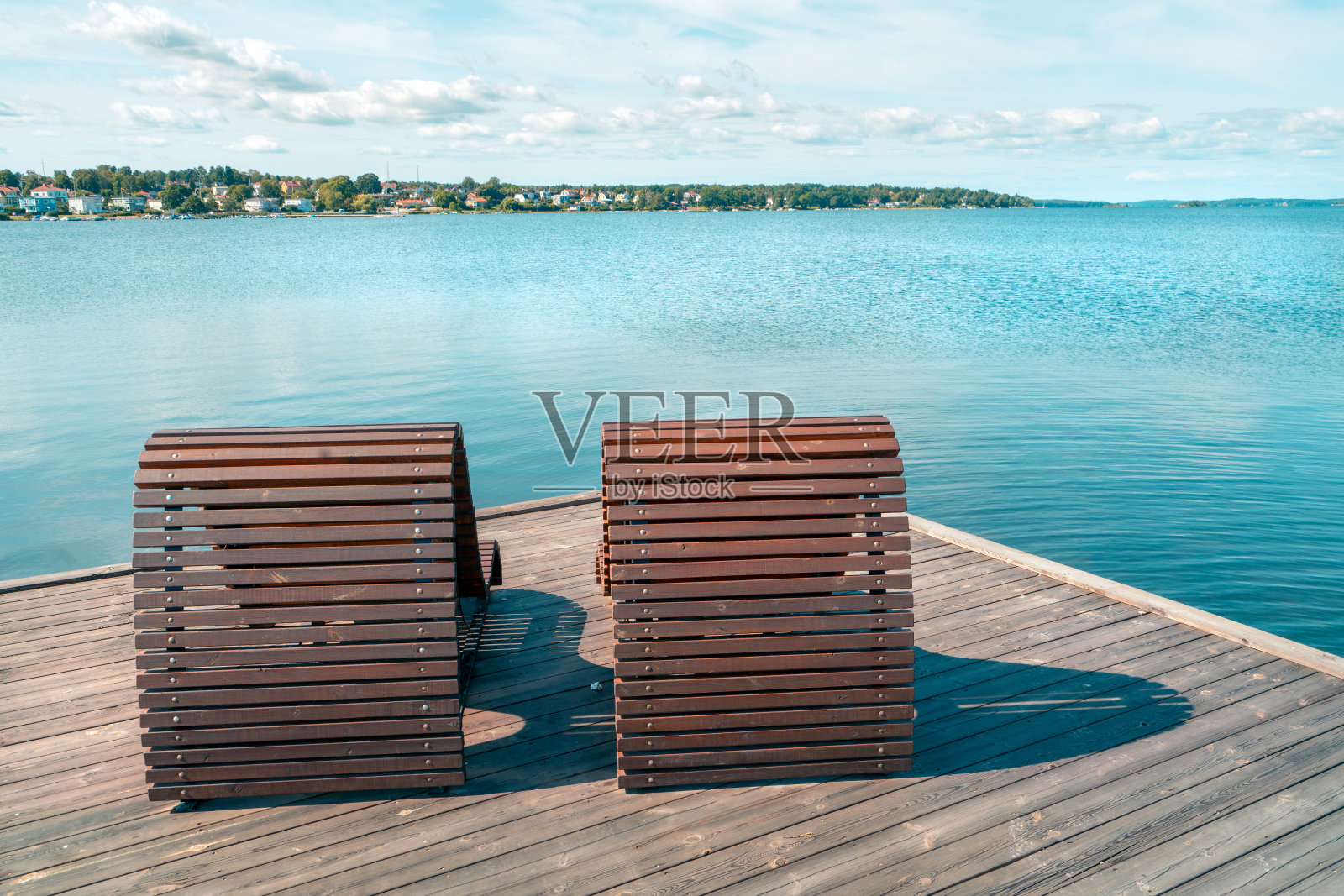 两张木制沙滩床或椅子放在海边的木制码头上，以城市景观为背景。晴朗的夏日，瑞典南部的维斯特维克，波罗的海旁。在海边度过暑假。照片摄影图片