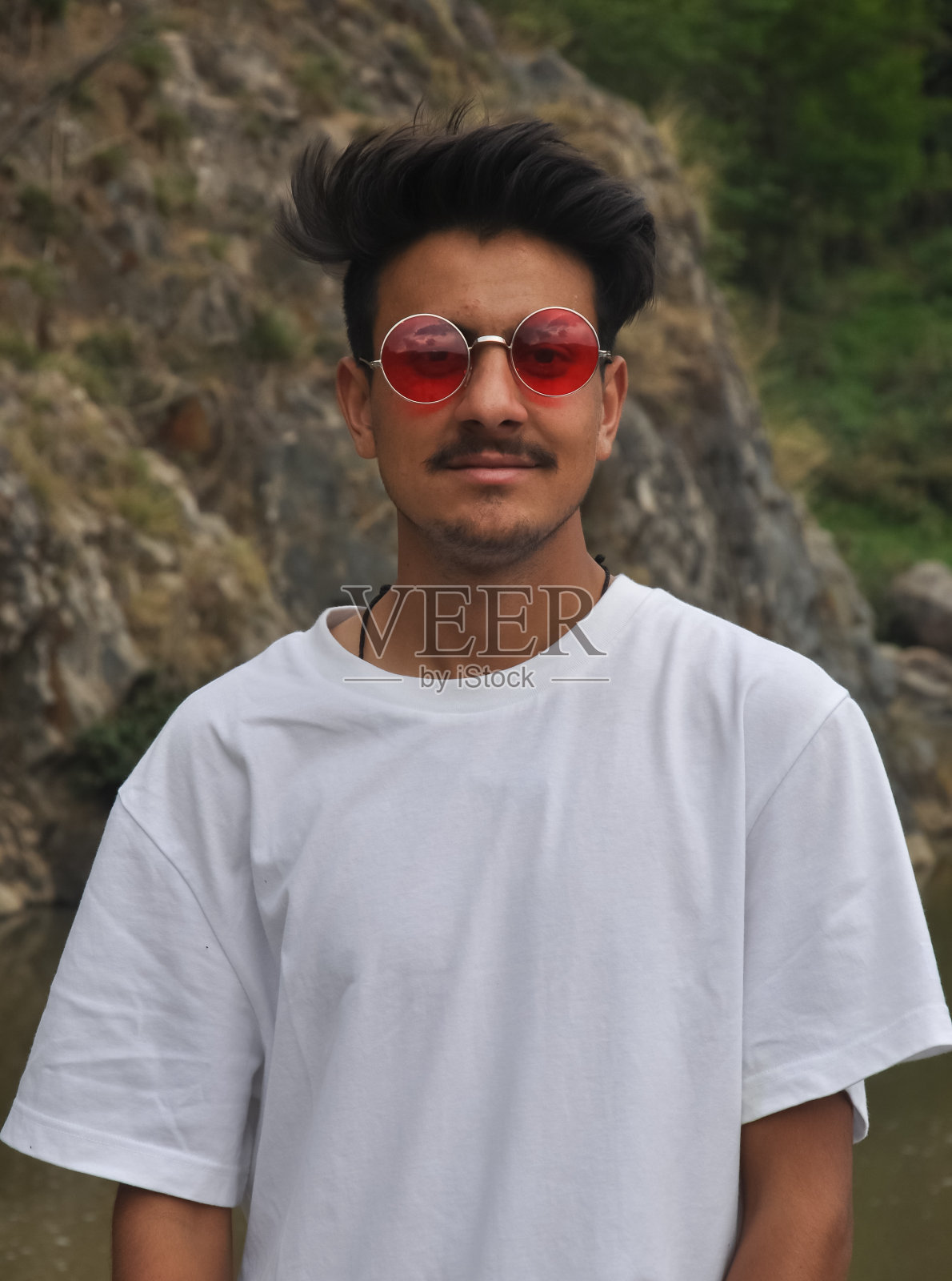一个英俊的北印度年轻人站在户外看着相机的肖像，一个穿着白色t恤和红色太阳镜的人照片摄影图片