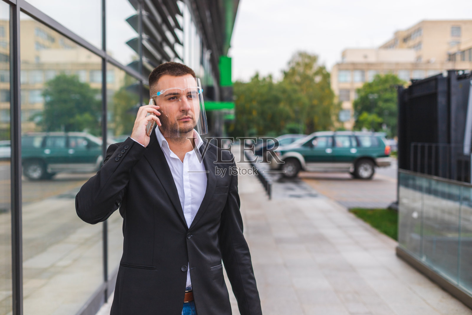 由于冠状病毒大流行，年轻英俊的白人商人戴着面罩在机场外打电话照片摄影图片
