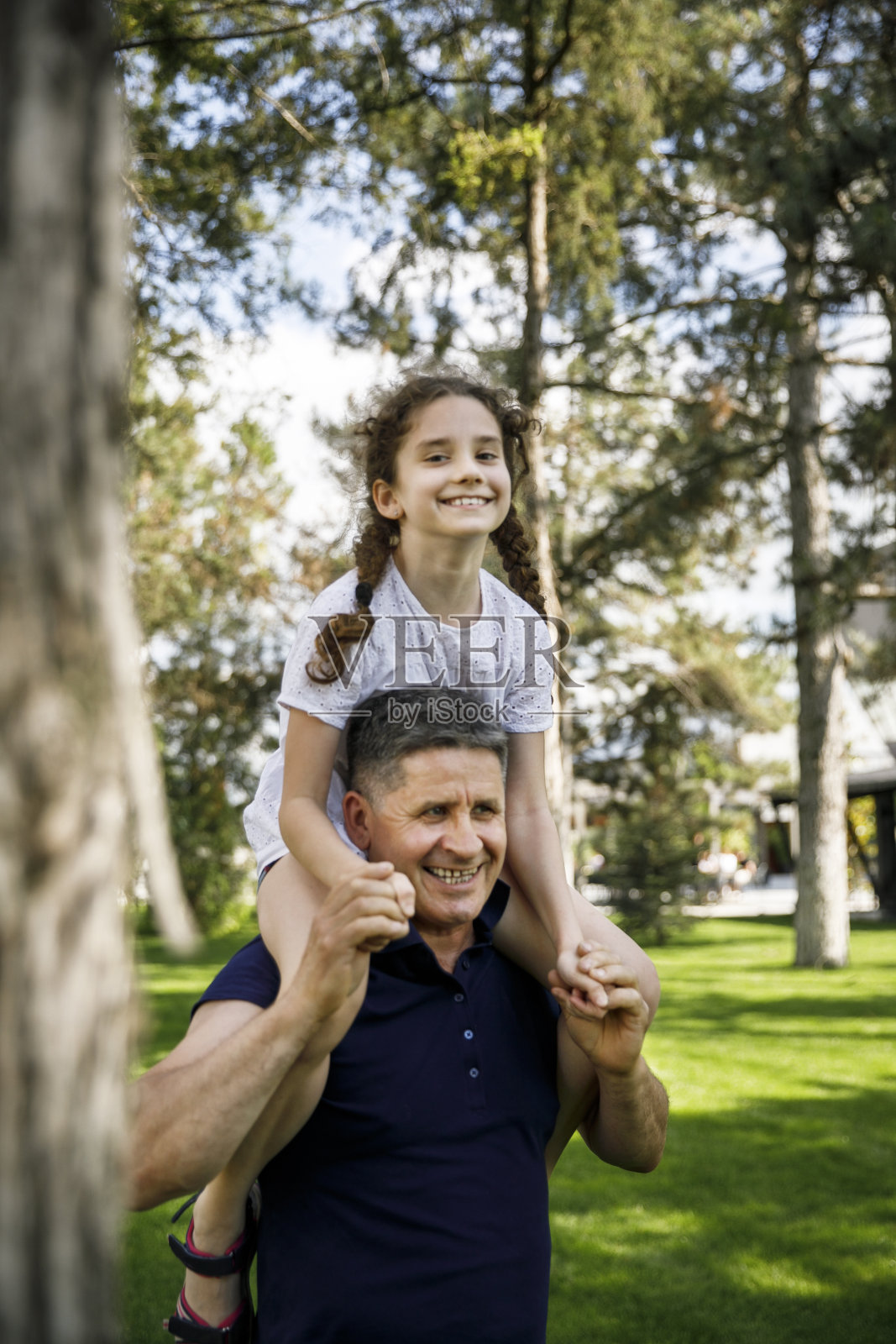 一个爷爷抱着他的侄女在他的肩膀上，他享受一个美好的日子在自然中。垂直的观点。照片摄影图片